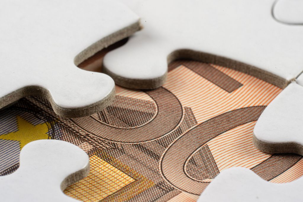 Detailed macro view of white puzzle pieces partially covering a Euro banknote.